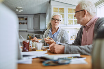 Senior couple talking while eating breakfast in the kitchen