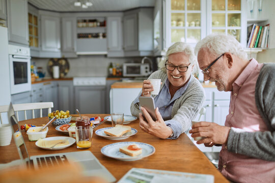 Senior couple using a smartphone and having breakfast in the morning in the kitchen