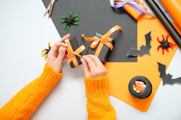 Woman with different decorations tying bows on gift boxes for Halloween against white background