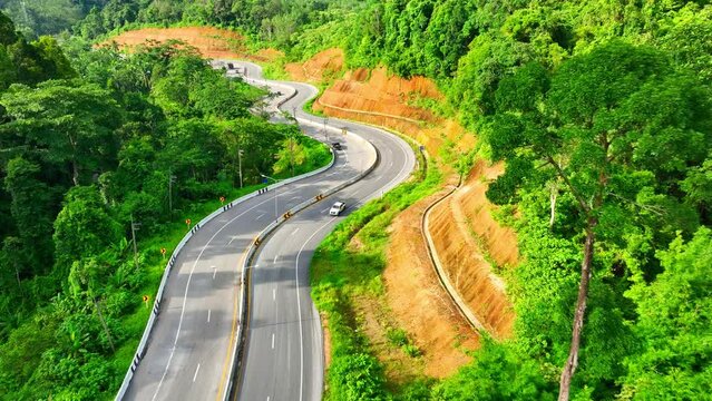 The mesmerizing beauty of Ranong Province, Thailand, as the drone glides above a meandering road cutting through lush tropical rainforests. A captivating journey through nature's paradise awaits.

