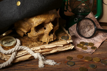 Human skull with pirate hat, old manuscripts, world map and travel equipment on brown wooden background