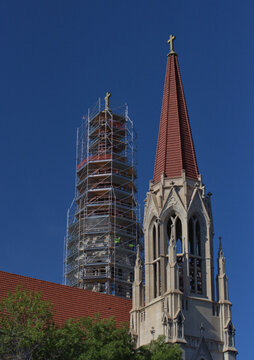 Construction workers, in green and doing repair work, look small on the array of metal scaffolding that surrounds one of two steeples on a cathedral. The crosses on top are 12 feet high.