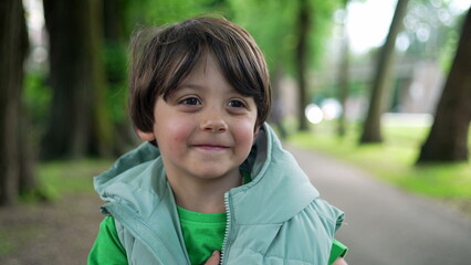 Portrait of a cute little boy standing outside at park smiling at camera and playing with hoodie jacket. Adorable expression