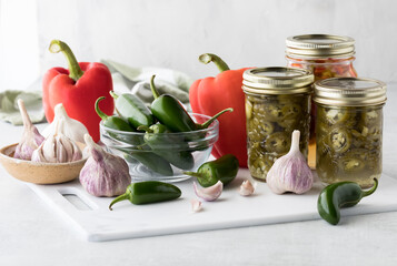 Canned jars of peppers with fresh jalapeno and red bell peppers beside.