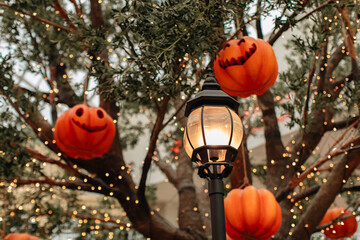 Bright pumpkin with a scary Halloween face hanging on a tree with garlands. Background for...