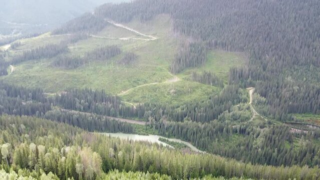 Aerial Landscape 90 Degree Down Tilt to Highway with Cars Driving. Slow tilt of mountains, terrain, trees, forest, sky, clouds, sun, lake, trail, green, snow on mountain peaks, stream, vehicles.