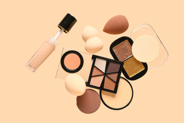 Flying makeup sponges and different cosmetics on color background