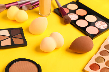 Set of makeup sponges and cosmetics on yellow background, closeup