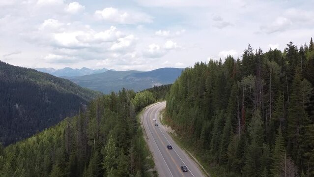 Highway Aerial Landscape View of Cars Driving by on Road Surrounded by Nature. Drone ascends overlooking a highway that is surrounded by mountains and a valley. 
