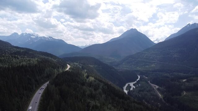 Drone Aerial Horizontal Down Motion Nature Shot of Highway  Valley in British Columbia Beaver Canada, Kinbasket Lake
View of Forest, Trees, Highway, Cars Driving, Mountains, Lake, Sky, Clouds