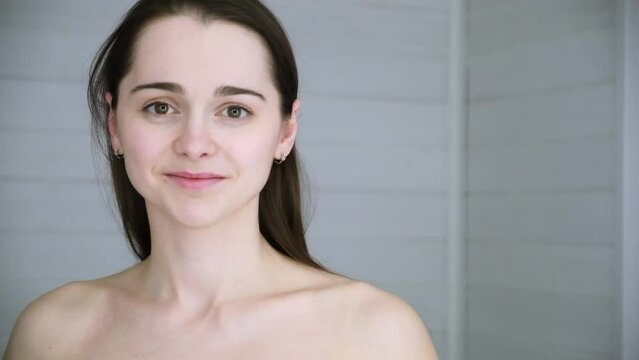 Beautiful smiling 30s woman fixes her hair with hands. A girl gets ready in the morning. Undyed brunette long straight hair. Without makeup. Beauty model. Healthy appearance hair and skin. Lifestyle.