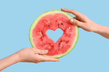 Woman holding slice of ripe watermelon with heart on blue background