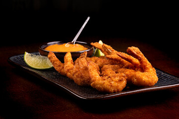 tapas portion of breaded prawns with sauce and slices of lemon on a black background