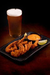 tapas portion of breaded prawns with sauce and lemon slices and chilled pint of lager beer on wooden table at an angle
