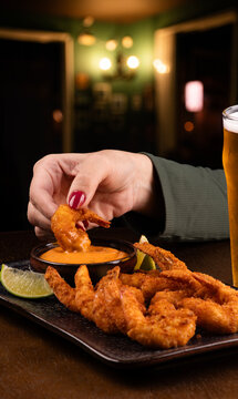 woman dipping prawns dipped in sauce at pub with chilled pint of lager beer with blurred pub in the background