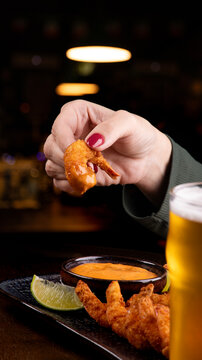 woman tasting breaded shrimp at the pub with a cold pint of lager beer with blurred pub in the background