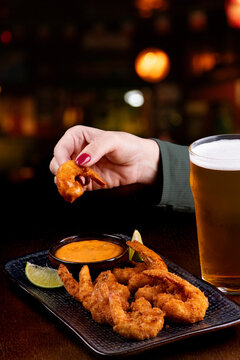 woman tasting breaded shrimp in pub sauce with chilled pint of lager beer with blurred pub in the background