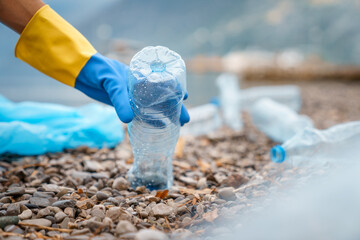 Focus on foreground photo of plastic bottle and human hand wearing blue glove during cleaning beach.