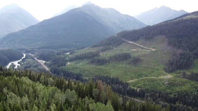 Quick to Slow Upward Aerial Drone Shot of Treed Mountain Valley in Canada. Lush greenery, tranquil forest, and majestic peaks converge in a picturesque valley, a natural wonderland to behold.
