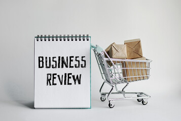 A notebook with the inscription BUSINESS REVIEW. With a decorative grocery cart along with small packaged mailboxes in the background. Lettering content matters for business, sales, and marketing. 