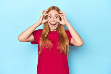 Fototapeta premium Redhead young woman on blue background keeping eyes opened to find a success opportunity.
