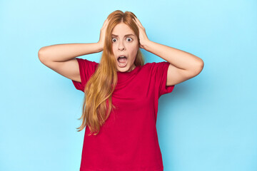 Redhead young woman on blue background screaming, very excited, passionate, satisfied with something.