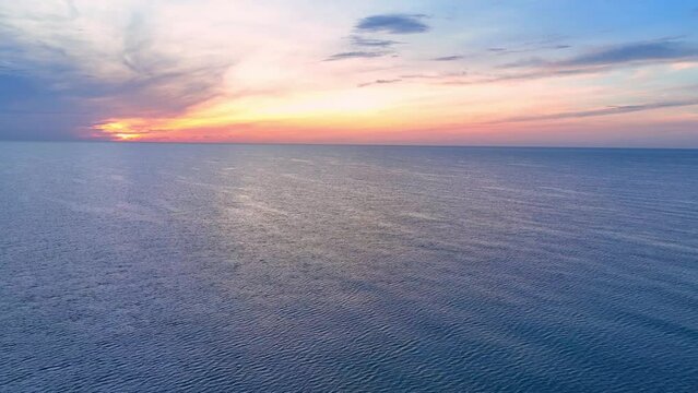 The sun begins its descent towards the horizon, painting the sky with hues of orange, pink, and gold, a breathtaking scene unfolds from the vantage point of a drone's aerial view above the sea.
