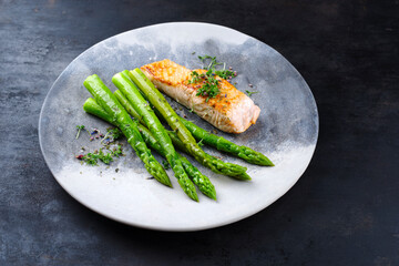 Traditionell glasierter grüner Spargel mit Lachs Filet und Kräuter serviert als Nahaufnahme auf einem Design Teller mit Textfreiraum