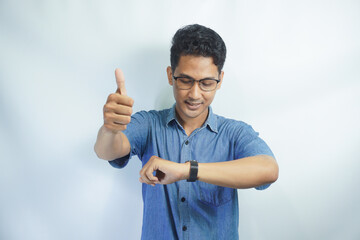 Fototapeta premium Portrait of an Asian man wearing a blue shirt smiling looking at his watch on a white background