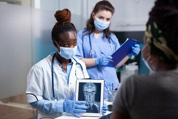 Radiologist and nurse delivering medical exam results to patient using x-ray cervical vertebrae ct scan to diagnose bone injury. Doctor medical checkup visit in sanitary sterile clinic