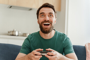 Portrait of excited handsome bearded male gamer playing video game, holding joystick