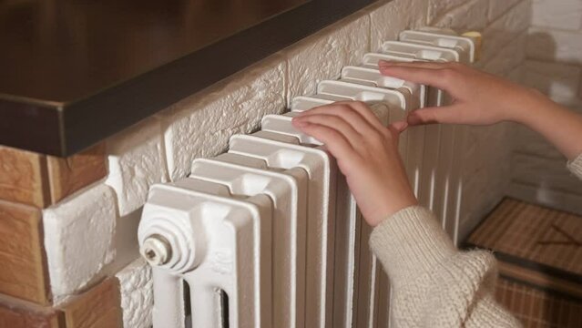 Child hands on central heating radiator. A view of little hands warming on the white radiator at home.