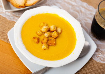 In deep ceramic plate, delicate cream soup is mashed from seasonal farm vegetables with addition of crispy small crackers.