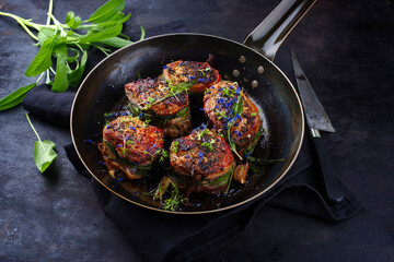 Traditionelle gebratene Fillet Medaillons vom Kalb mit Speck Mantel und Salbei Blätter in Butter Sauce serviert als close-up in einer rustikalen schmiedeeisernen Bratpfanne