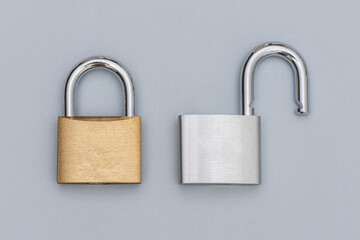 Fototapeta premium Locked golden and unlocked silver padlock on the gray background.