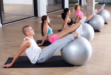 Group of active people engaged in Pilates in the gym performs an exercise sitting on a sports mat,...