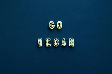 Close-up view of ‘Go vegan’ slogan made up of alphabet pasta against dark blue background  