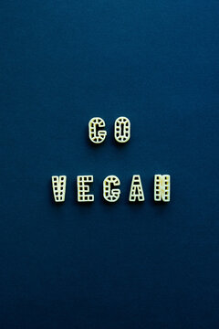 Naklejki Alphabet pasta forming inspirational lettering ‘Go vegan’ against dark blue background 