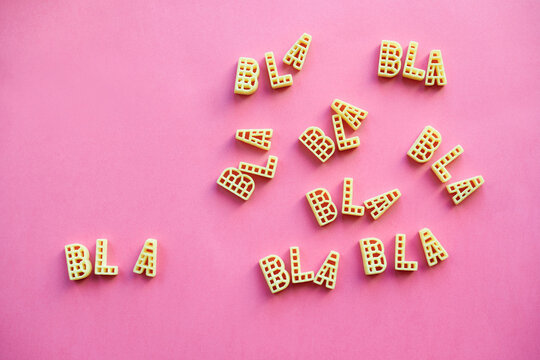 Alphabet pasta forming multiple words &lsquo;bla&rsquo; lying on pink paper background  