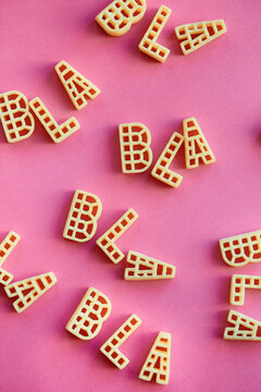 Close-up view of multiple words &lsquo;bla&rsquo; made up of alphabet pasta on pink background 