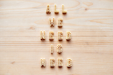 Close-up view of alphabet pasta forming creative remade quote ‘All we need is weed’ laid out on wooden table 