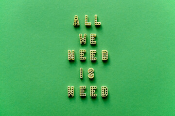 Close-up view of creative transformed quote ‘All we need is weed’ made up of alphabet pasta letters against green background 