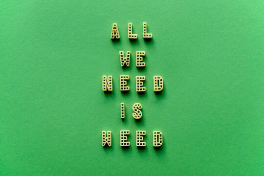 Naklejki Close-up view of creative transformed quote ‘All we need is weed’ made up of alphabet pasta letters against green background 