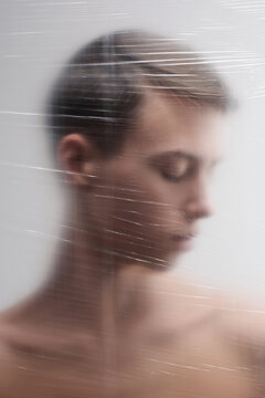 Conceptual portrait of unhappy young man standing behind plastic film with his eyes closed and head turned 