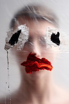 Conceptual photo of unrecognizable young man standing behind plastic film with ugly eyes and lips painted on it  