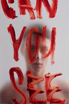 Conceptual picture of gloomy young man standing behind plastic film with inscription Can you see written with red lipstick on foreground  