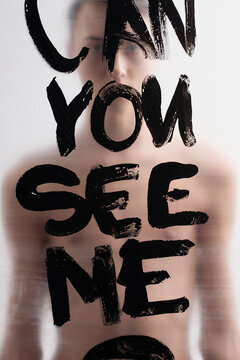Conceptual photo of cheerless young man standing behind plastic film with inscription Can you see me and looking at camera  