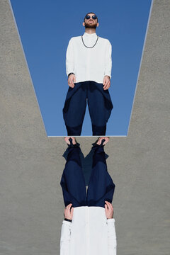Conceptual shot of young fashionable man in sunglasses being reflected in mirror against clear blue sky background  