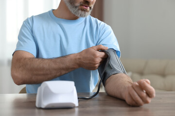 Man measuring blood pressure at table indoors, closeup