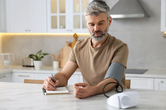 Man measuring blood pressure at table indoors